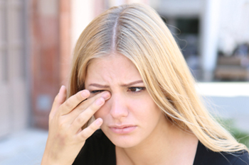 young woman rubbing eyes outside